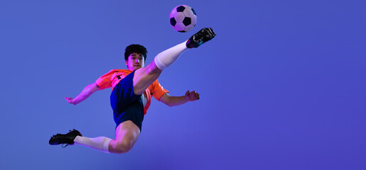 Fototapeta na wymiar Studio shot of male professional football, soccer player practicing with ball isolated on purple background. Concept of sport, match, active lifestyle, goal and hobby