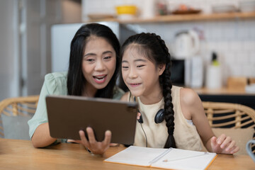portrait of cheerful asian mother and daughter using digital tablet in kitchen at home