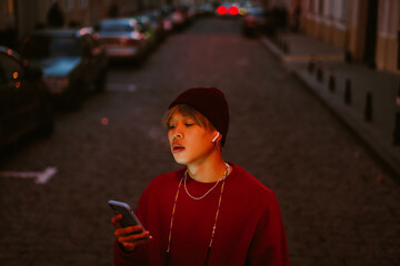 Asian boy using mobile phone while smoking at city street