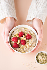 Oatmeal porridge bowl with berries and nuts in woman's hands. Concept of healthy vegan diet, clean...