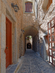 Fototapeta na wymiar A cobblestone alley between picturesque old stone houses with reddish doors and windiws. Pirgi, Chios island, Greece