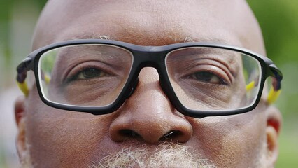 Close portrait of senior black man in glasses opening his eyes and looking to camera with a smile