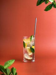 Cold lemonade with ice, lemons and herbs on a brown background. Metal straw for a cocktail. Minimalism. Branches of trees in the corner of the frame. Copy space. Vertical