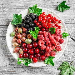 Variety of summer berries in a plate on a rustic wooden background, top view