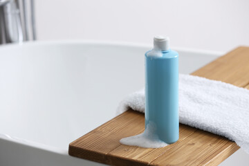 Bottle of bubble bath with foam and towel on tub in bathroom, space for text