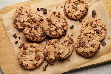 Many delicious chocolate chip cookies on wooden board, flat lay
