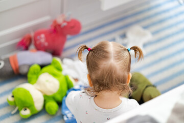 baby girl with two pigtails have fun with plush toys at natural home background, view from behind - obrazy, fototapety, plakaty
