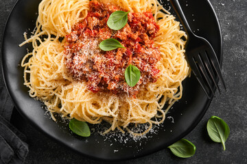 Classic spaghetti pasta Bolognese. Tasty appetizing italian spaghetti with bolognese sauce, tomato sauce, cheese parmesan and basil on black plate on dark slate, stone or concrete table background.