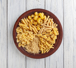Different types and shapes of Italian pasta in ceramic plate on white wooden background