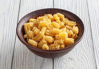 Uncooked radiatori pasta in ceramic bowl on white wooden background