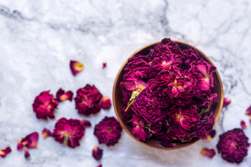 dried organic pink rose buds in wooden bowl on white table.