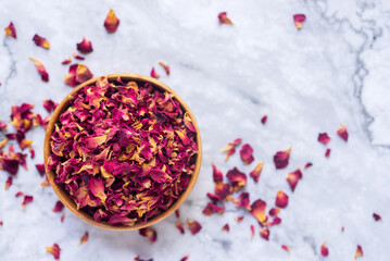 dried organic pink rose petals in wooden bowl on white table.