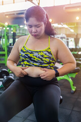 Fat woman hand holding excessive belly fat isolated on gym background, Obese woman's fingers measuring belly fat