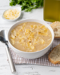 Onion soup with cheese in a bowl with bread slices and seasonings over wooden table