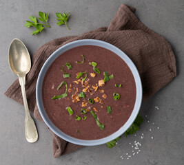 Black bean soup in a bowl with seasoning over stone background