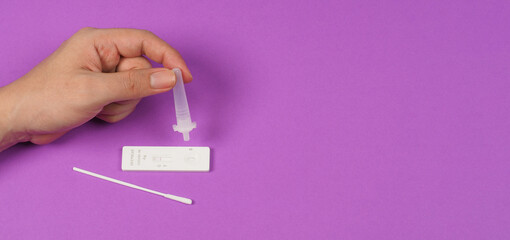 Obraz premium A hand is holding an antigen extraction tube and antigen test device, Sterlized Swab on the floor with a violet background..