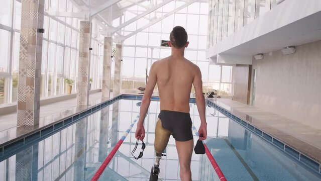 View From The Bach Of A Disabled Male Swimmer With A Prosthetic Leg Standing In Front Of A Pool.