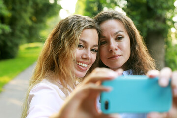 mature mother and adult daughter are doing selfie by mobile phone in summer park