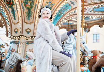 Fototapeta na wymiar Laughing young woman at the winter fair riding a horse, carousel