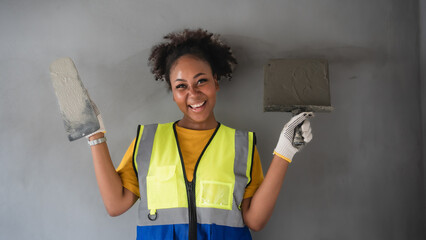 Portrait of an attractive African-American woman standing with plastering tool. The back is grey cement wall. Female worker,wall decoration specialist.Smiling confidently. expert skim coat,plastering