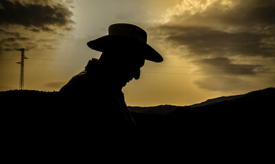 Silhouette of adult man in cowboy hat standing in desert against sky. Almeria, Spain