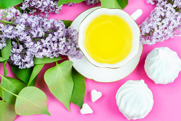 A mug of green tea, marshmallows, sugar cubes, and a blooming branch of lilac on a bright pink background. Good morning! The concept of the celebration. Birthday greetings, March 8, mother's day.