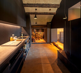 Modern kitchen front view in a renovated mountain chalet. At the back there is the pantry with hanging salami and ham and some bottles of wine