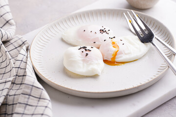 Three poached eggs with egg yolk dripping and black sesame seeds on a white plate on a marble board and silver forks