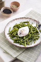 Obraz na płótnie Canvas Soft-boiled poached eggs with black sesame seeds on a cooked green beans on a plate with brown rim on a green checkered kitchen towel