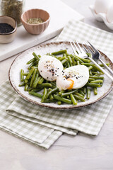 Soft-boiled poached eggs with black sesame seeds on a cooked green beans on a plate with brown rim on a green checkered kitchen towel