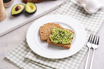 Slices of gluten-free sunflower seeds bread with avocado and sesame seeds on white plate on green checkered napkin