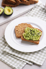 Slices of gluten-free sunflower seeds bread with avocado and sesame seeds on white plate on green checkered napkin
