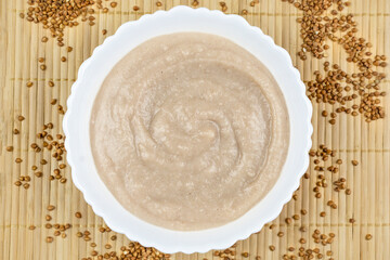 Buckwheat porridge for a baby from ground cereals in a white bowl on a brown bamboo background...