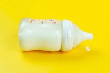 Baby bottle with milk formula on a bright yellow background. Artificial feeding of the baby.