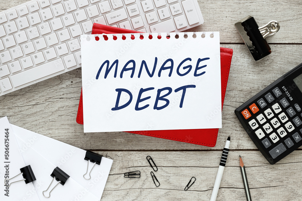Poster manage debt. text on a sheet of paper on a red notepad on a wooden background