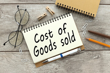 cost of goods sold . Business and finance concept. text on open notepad near glasses