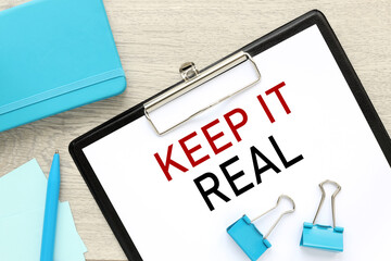 Keep It Real . text on paper on folder near blue notepad on gray background