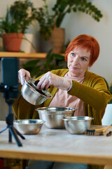 Mature woman using her mobile phone for streaming, she sitting at table and telling about planting