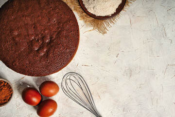 Top view on a round chocolate sponge cake or chiffon cake on baking paper so soft and delicious with ingredients: eggs, flour and cacao with copy space for text