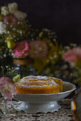 Bolo de fubá coberto de açúcar em cenário romântico, com flores ao redor.