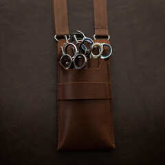 Professional shears scissors in leather case on leather brown background. Barbershop, concept.