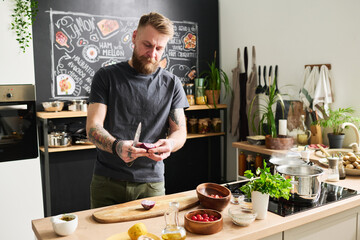 Portrait of handsome young adult Caucasian man with beard and moustache on face standing in kitchen...