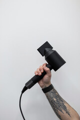 Male hand with a tattoo is holding a black modern hair dryer against a white background. Professional barber in a barber shop. Creative work