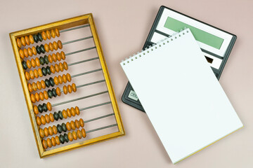 Old antique wooden abacus, modern calculator, notepad (notebook) with a blank page for writing on a beige background. Space for text. Progress in business, accounting, accounting.
