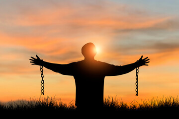 Silhouette of freedom young man standing alone with beautiful sky at sunset open both arms with chains on his arms. He felt free from the shackles tied to his arms.