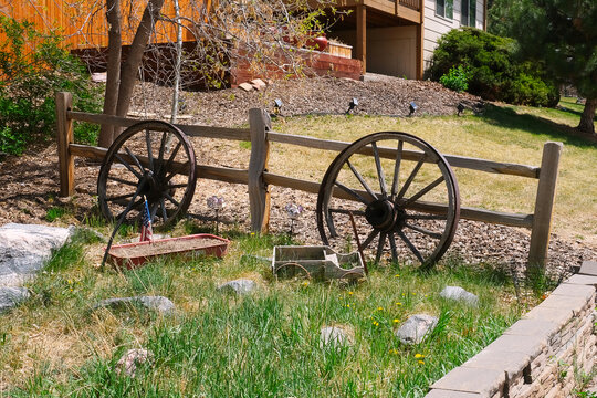 Farm, garden or front yard countryside decoration with old wooden cart wheels, small toy coach wagon, plant pot and American flag in grass with decorative rocks at fence photo.