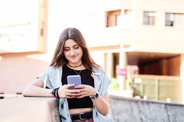 Happy woman using a smart phone in the street with an unfocused background