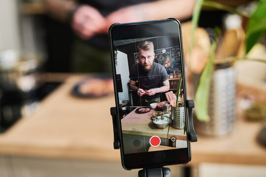 Horizontal selective focus close-up of food blogger filming content on smartphone camera using tripod