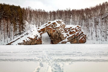 Winter landscape with a big stone, forest, sky from a frozen river