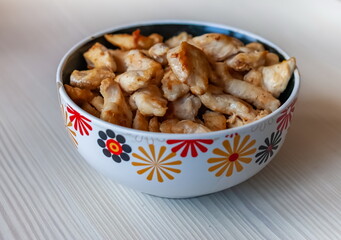 Pieces of fried chicken in a ceramic cup close-up on the background of a light kitchen table